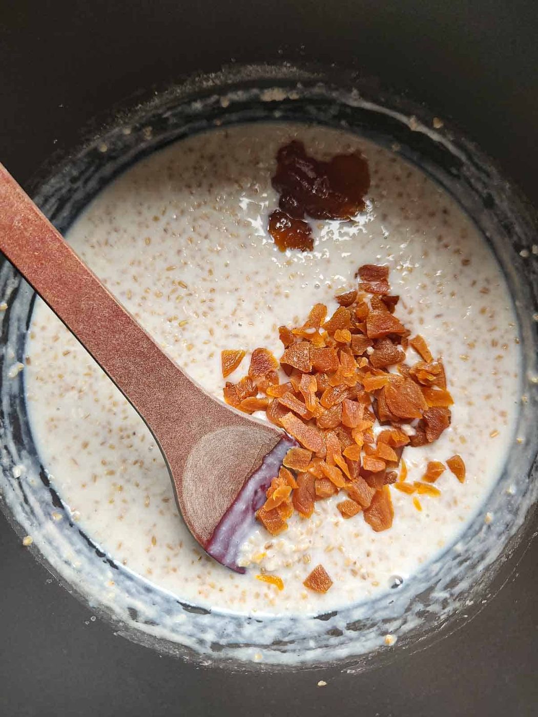Overview of oatmeal and apricots in a pot with a wooden spoon.