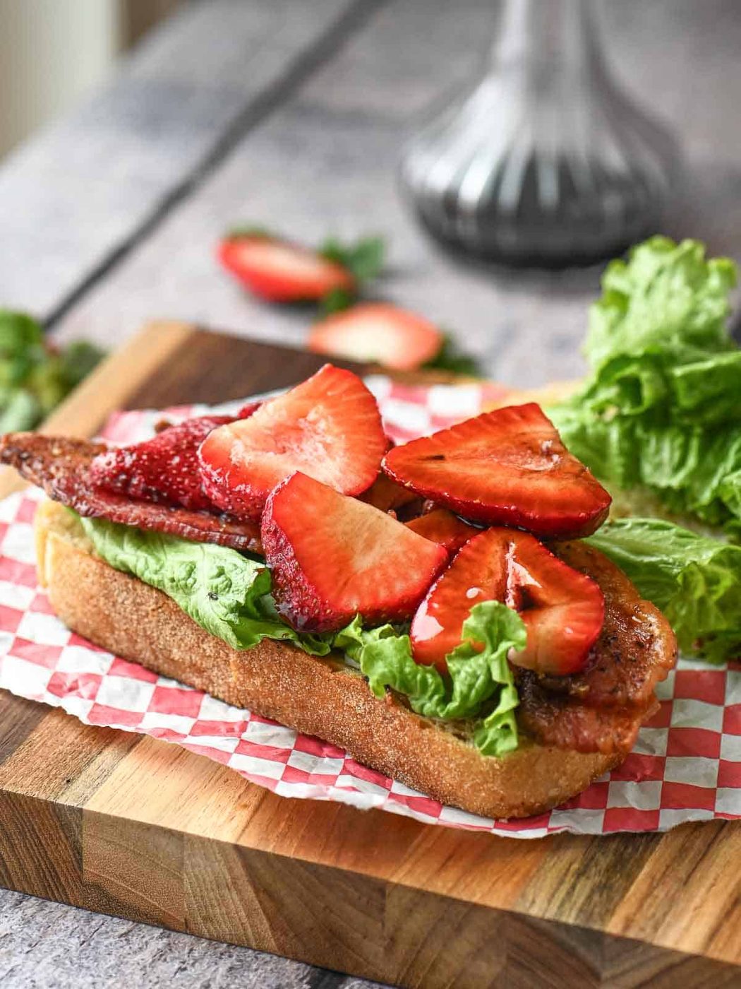 Strawberries on top of bread and lettuce on a cutting board.