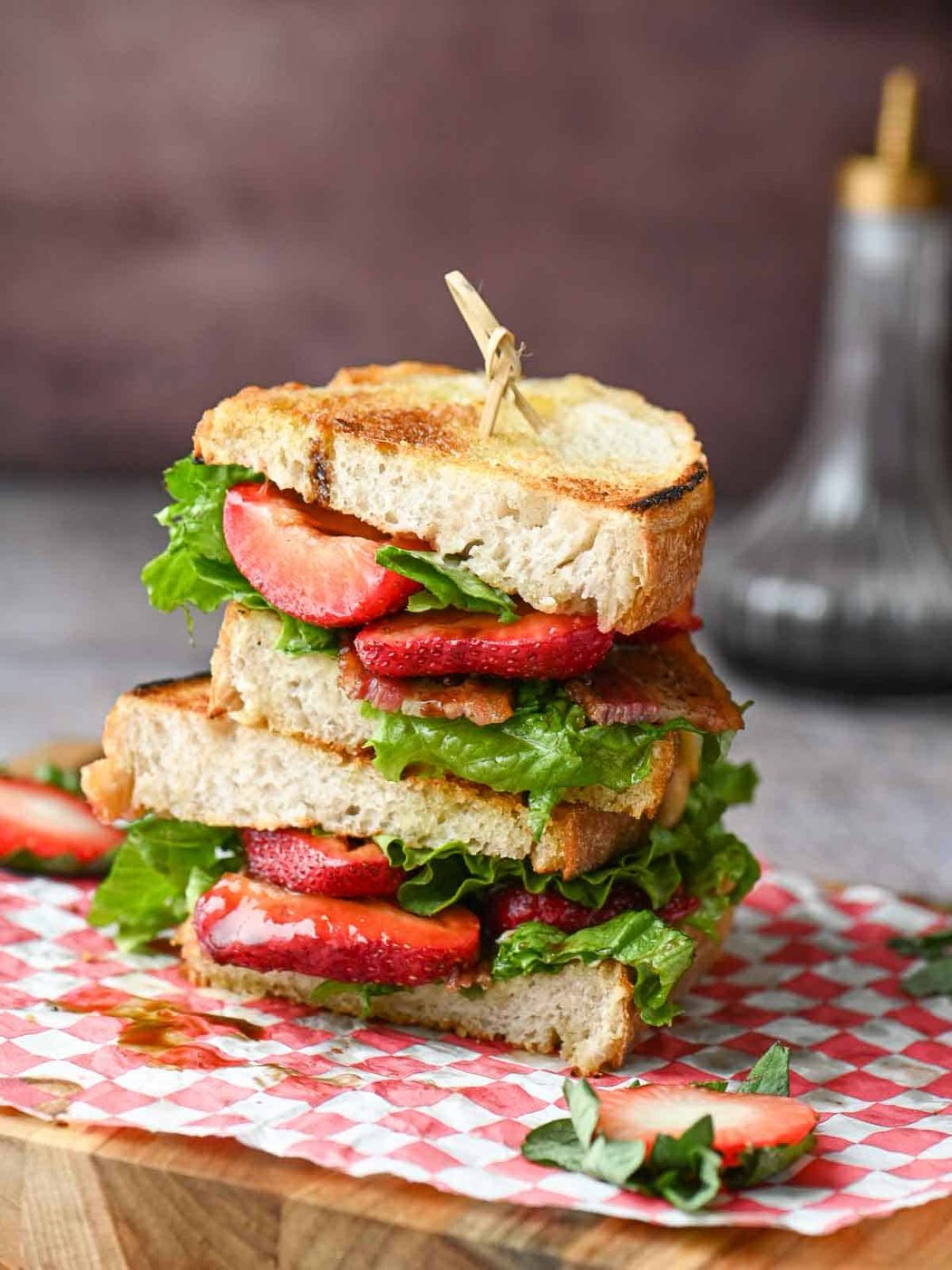 Two halves of a strawberry BLT with balsamic stacked on red checkered deli paper.