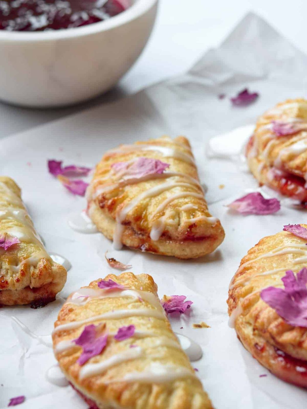 Strawberry mini pies on white parchment with strawberry jam in the background.