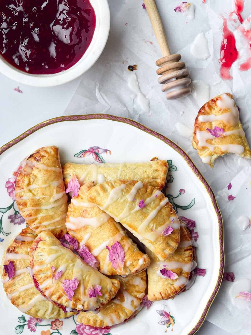 Overhead view of strawberry mini pies on a plate with rose glaze drizzled over parchment paper.