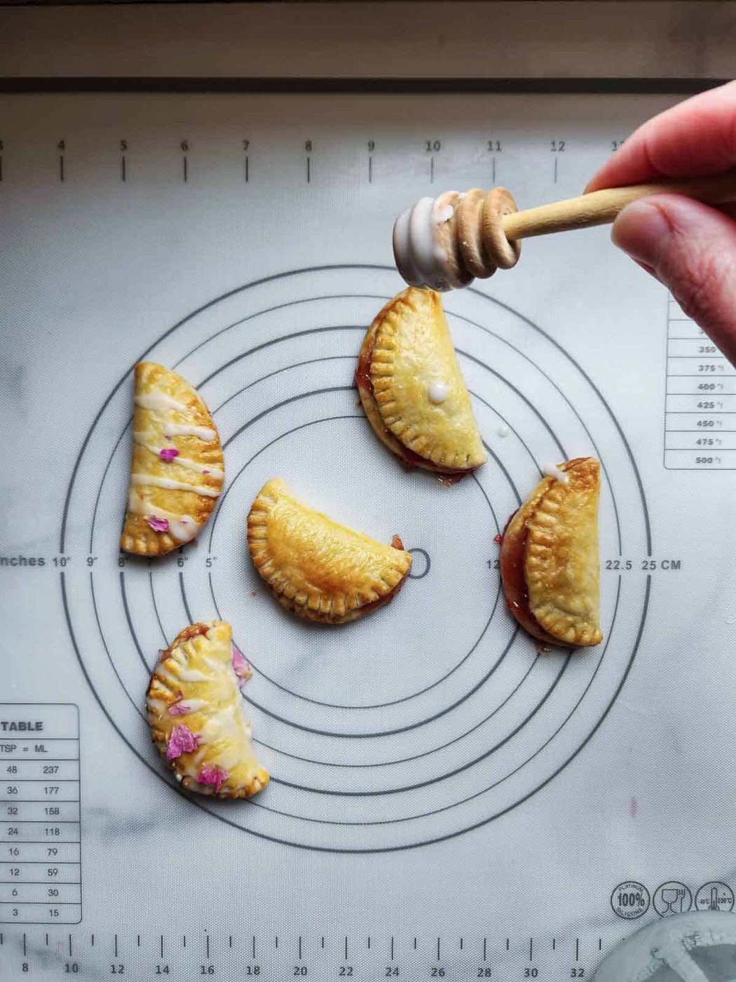 Drizzling rose glaze on top of strawberry mini pies.