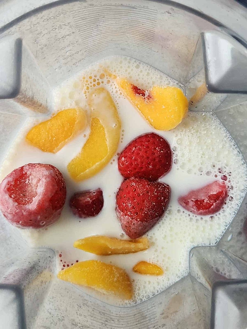 Overhead of milk and frozen fruit in a blender.