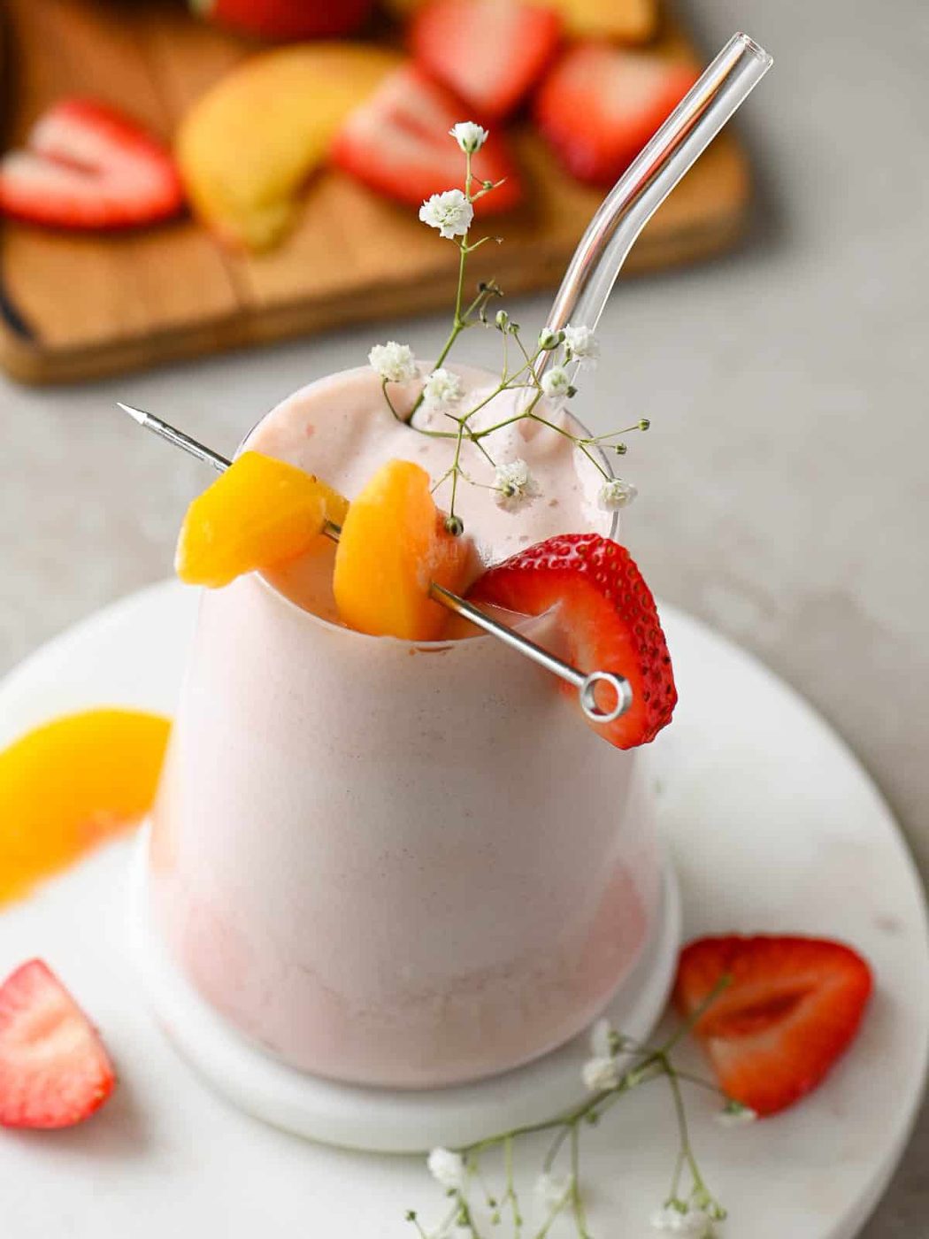 Strawberry peach smoothie in a clear glass with fruit on top.