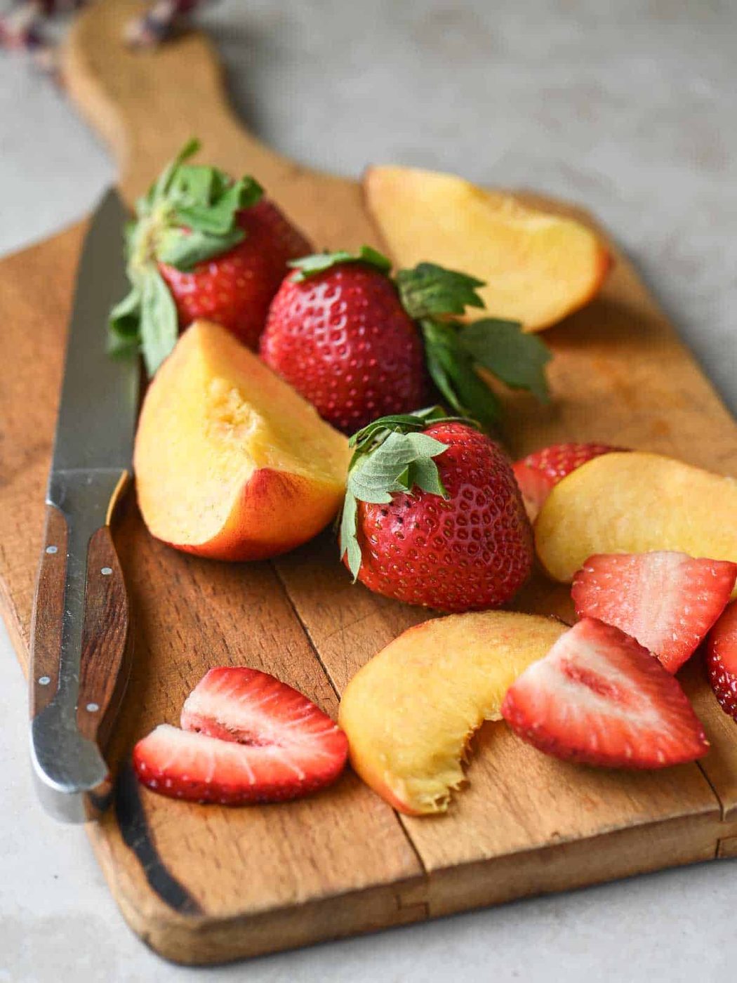 Sliced peaches and strawberries on a cutting board.