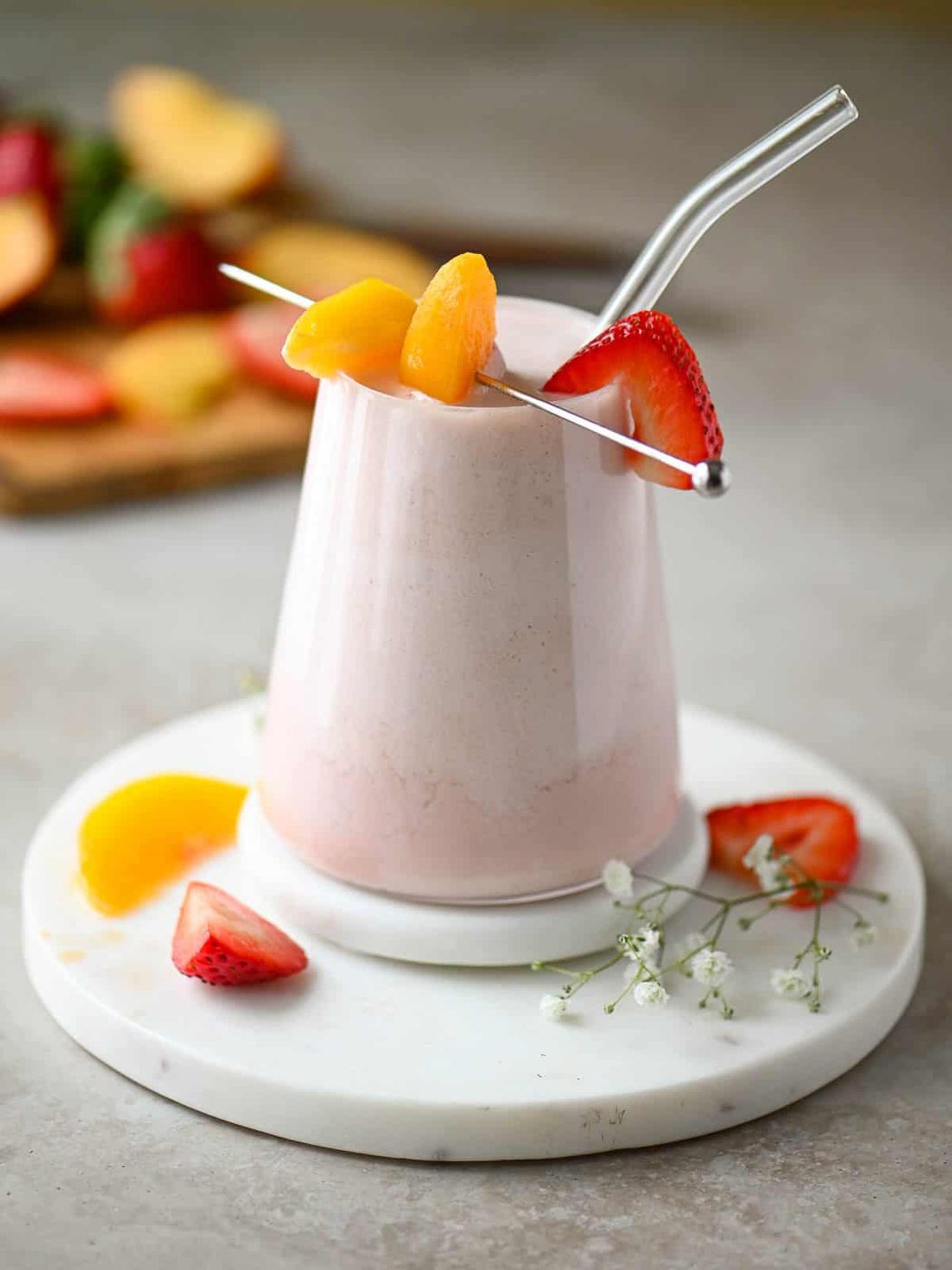 Eye level fruit smoothie with strawberries and peaches in the background.