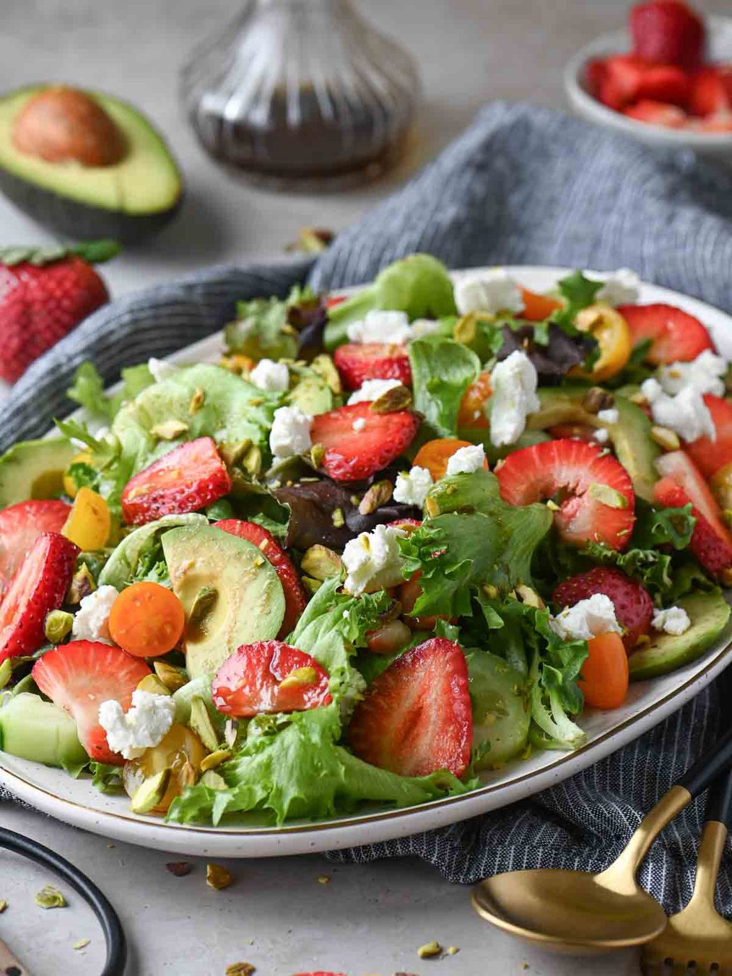 Angled view of a strawberry salad on an oval plate with vegetables around it.