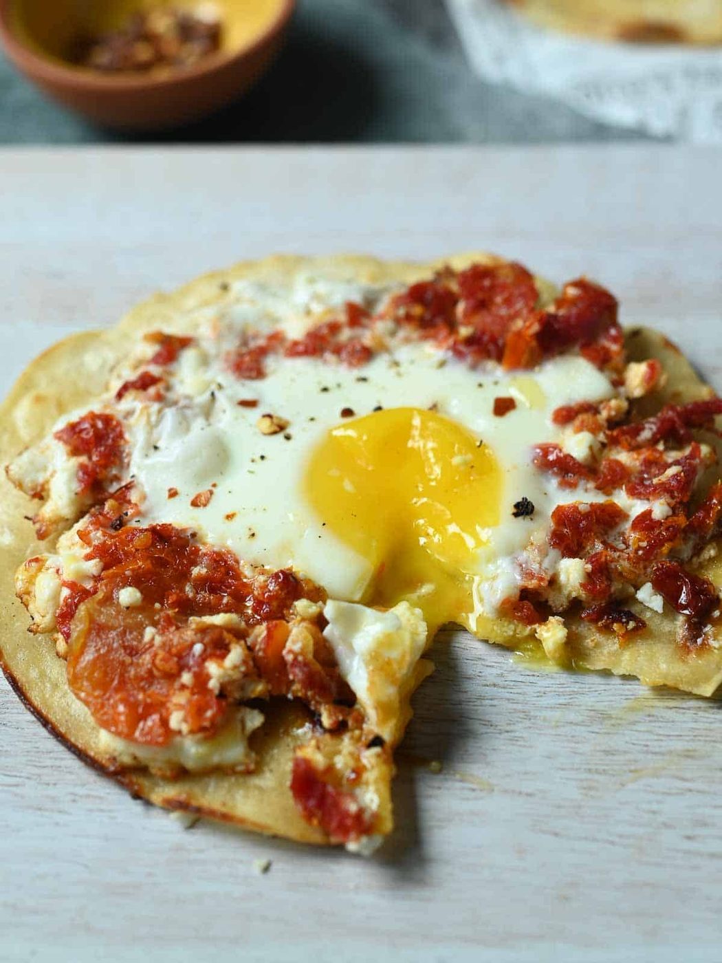 Sun-fried-tomato and feta fried egg on a cutting board with a piece cut out.