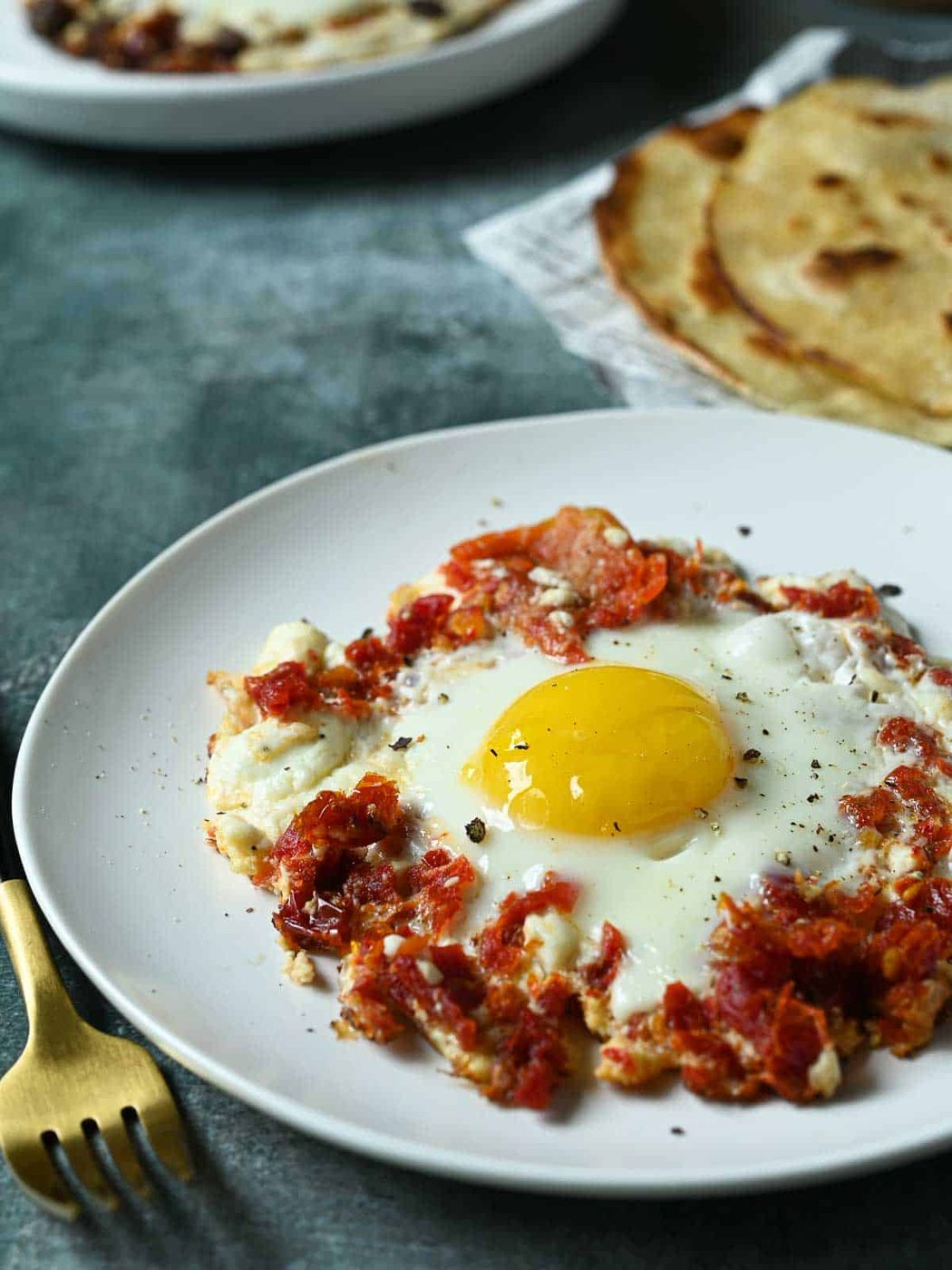 Tomato and feta fried egg on a white plate with bread in the background.