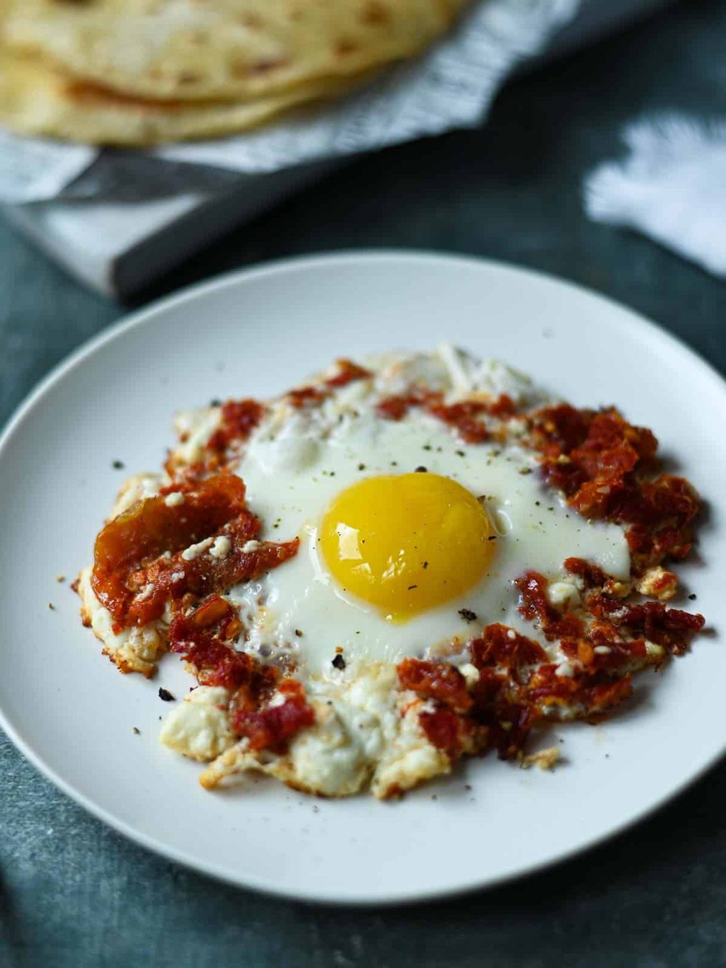 Sun-dried tomato and a fried egg on a white plate.