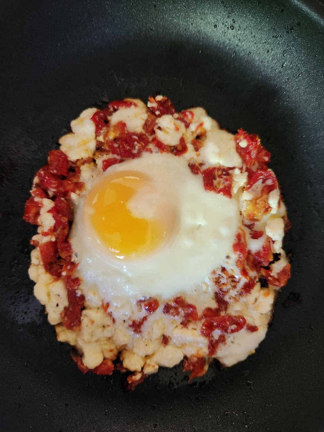 Fried egg in a skillet with tomatoes and feta.
