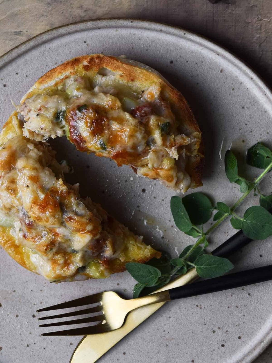Sun-dried tomato tuna melt, cut in half on a plate with a fork and knife.