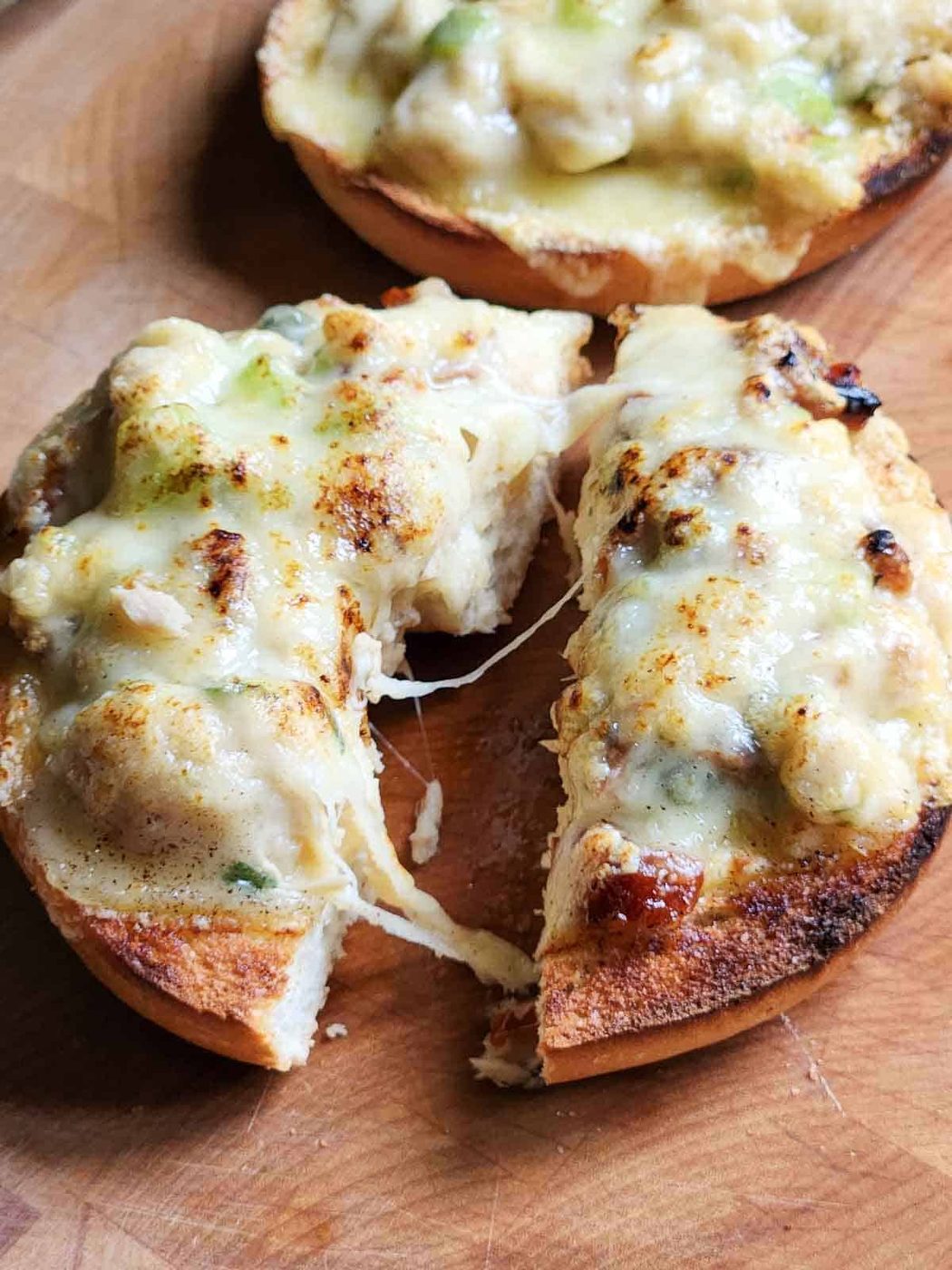 A tuna melt bagel cut in half with cheese pulled.