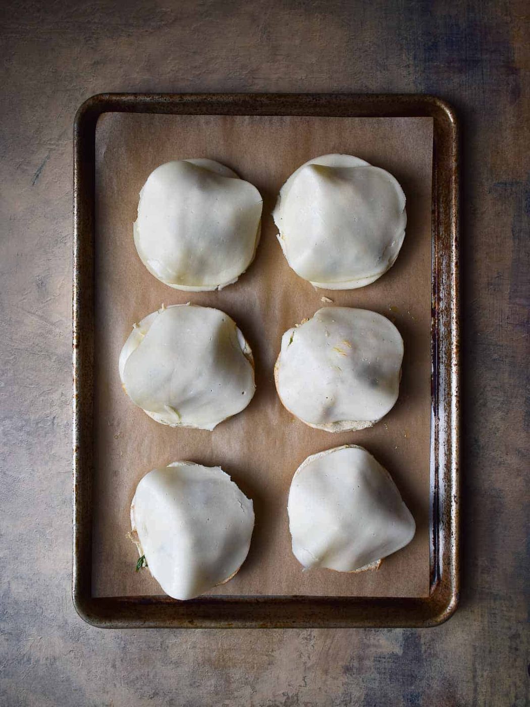 Six bagels with tuna and cheese on top on a baking sheet.