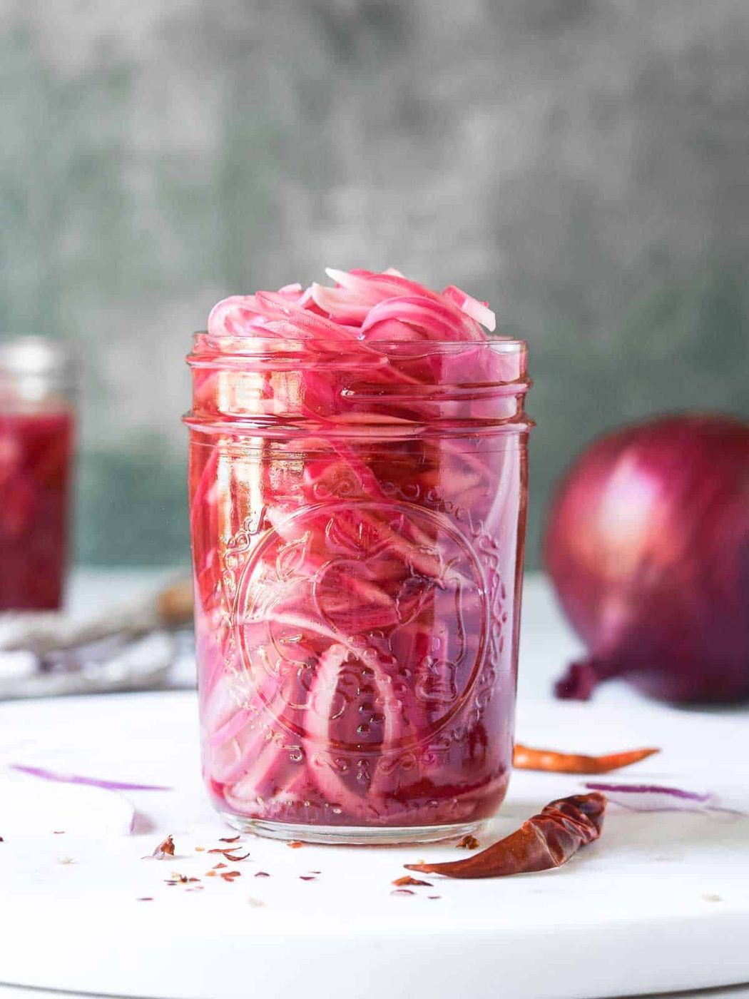 Pickled red onions in a clear mason jar on a white surface.