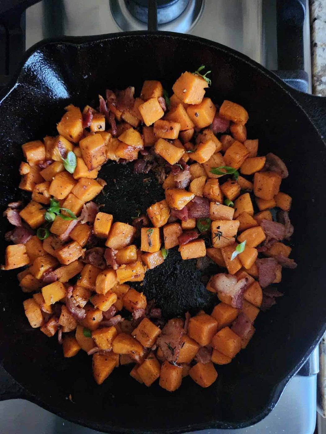 Sweet potato hash in a skillet with 2 wells in the middle for eggs.