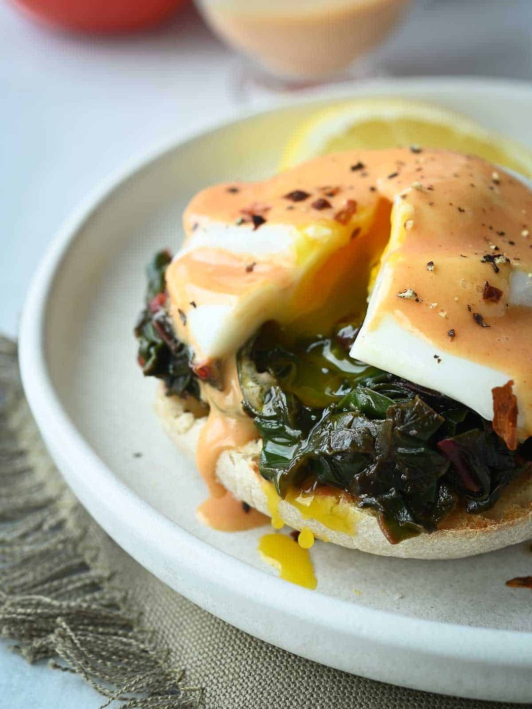 Eggs Florentine with a poached egg cut open and yolk dripping out on a white plate.