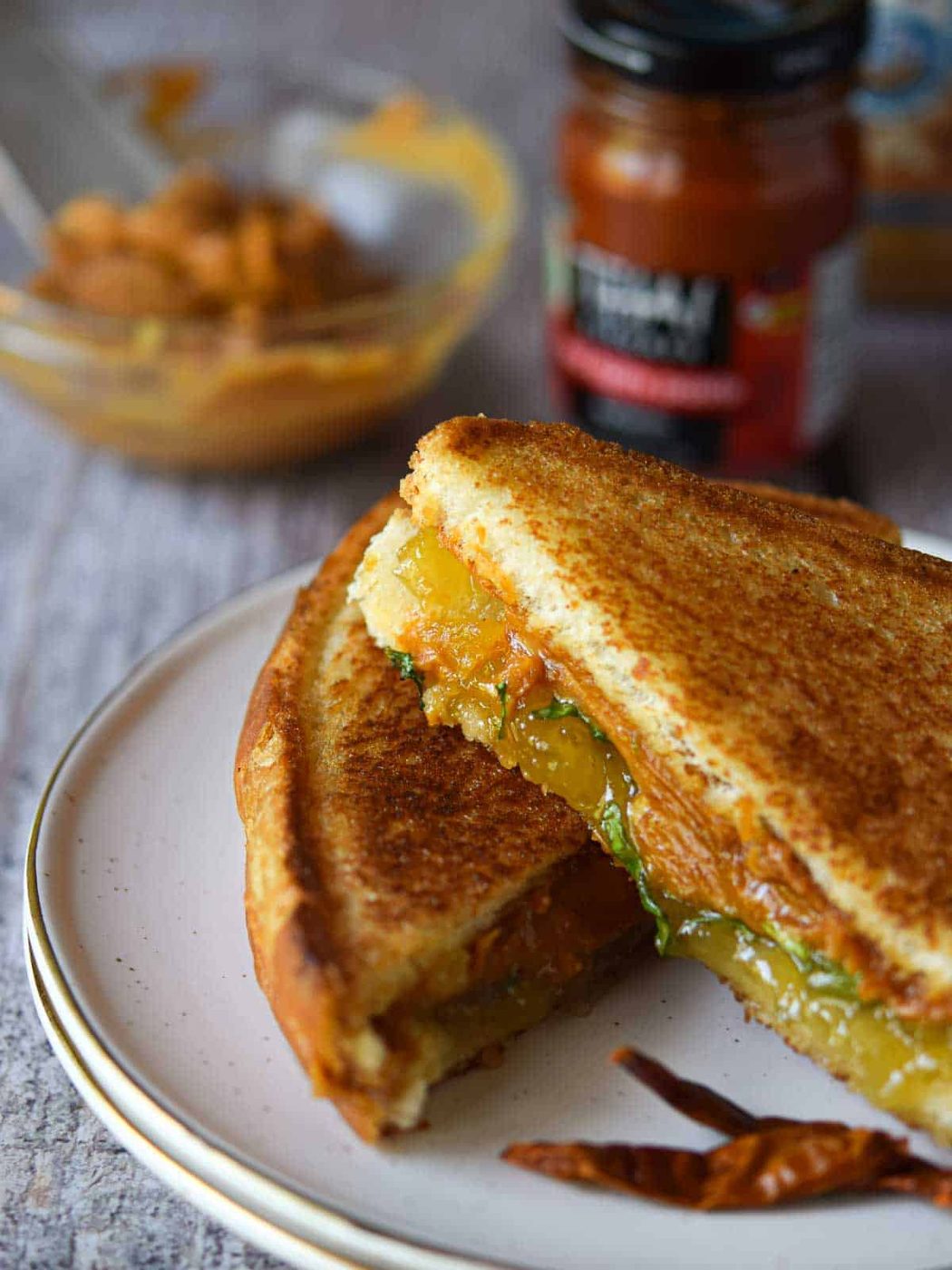Thai peanut butter sandwich cut and stacked on a plate with peanut butter in the background.