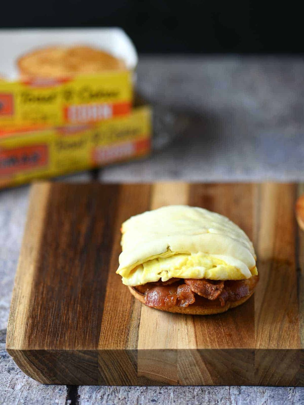 Egg, cheese, and bacon on a toaster cake on top of a wooden board.