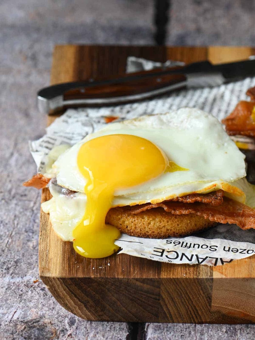 A drippy soft boiled egg over a toaster cake with bacon and cheese, served on a cutting board.