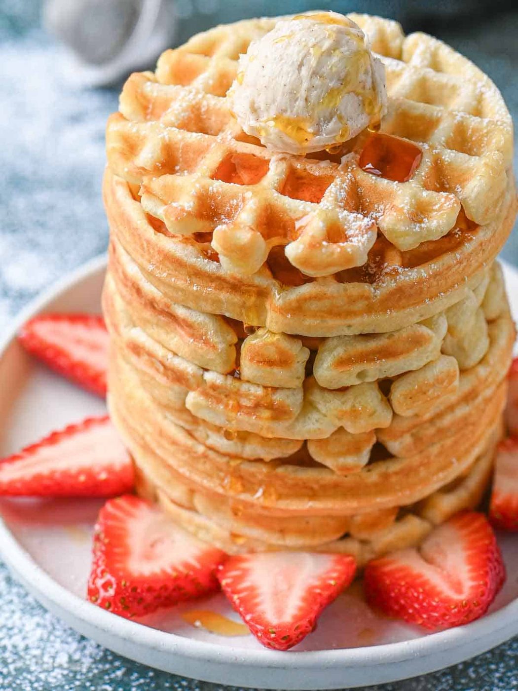 A tall stack of waffles with butter and strawberries.