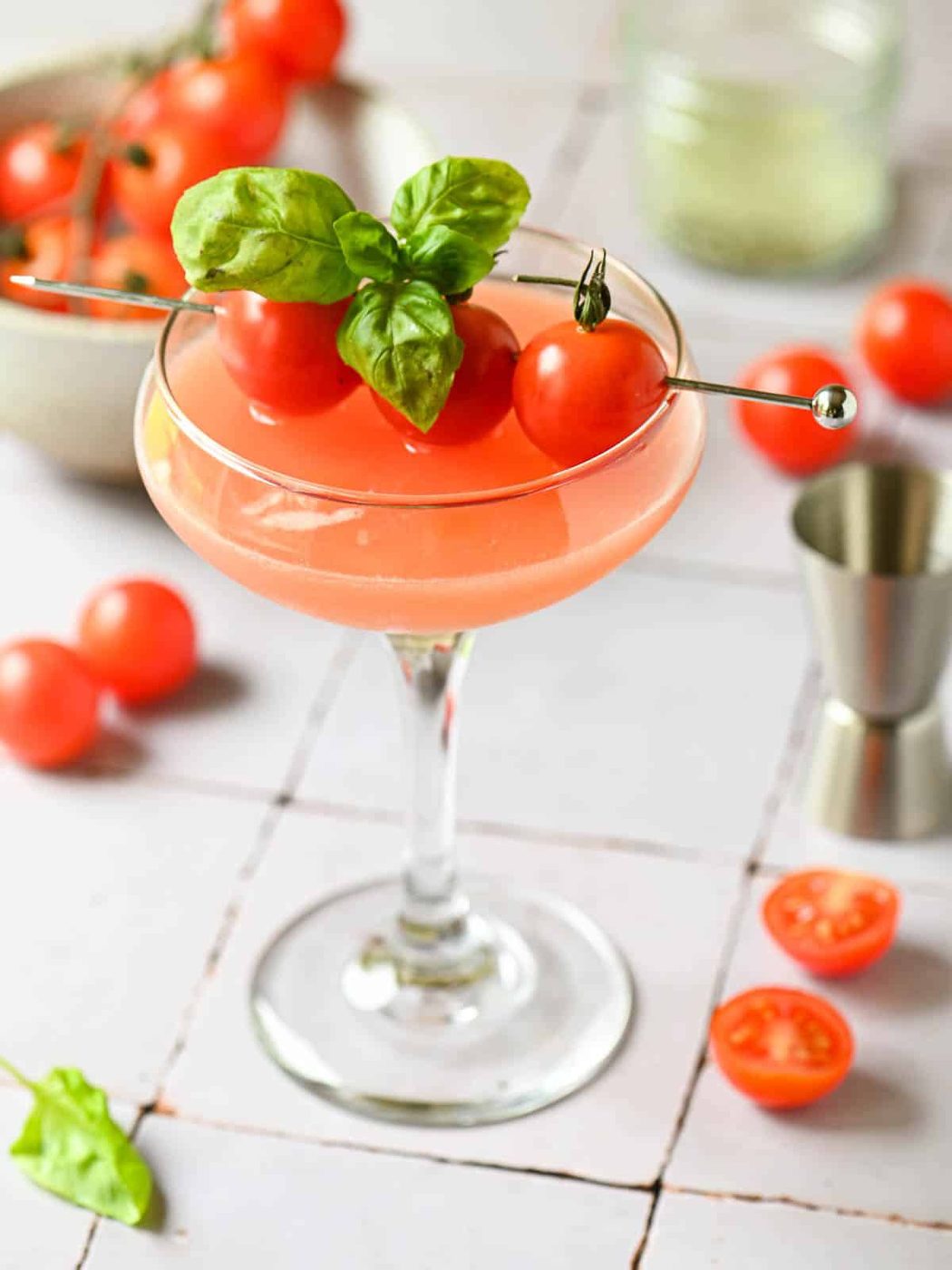 A tomato martini on a tiled surface with a cocktail shaker in the back.