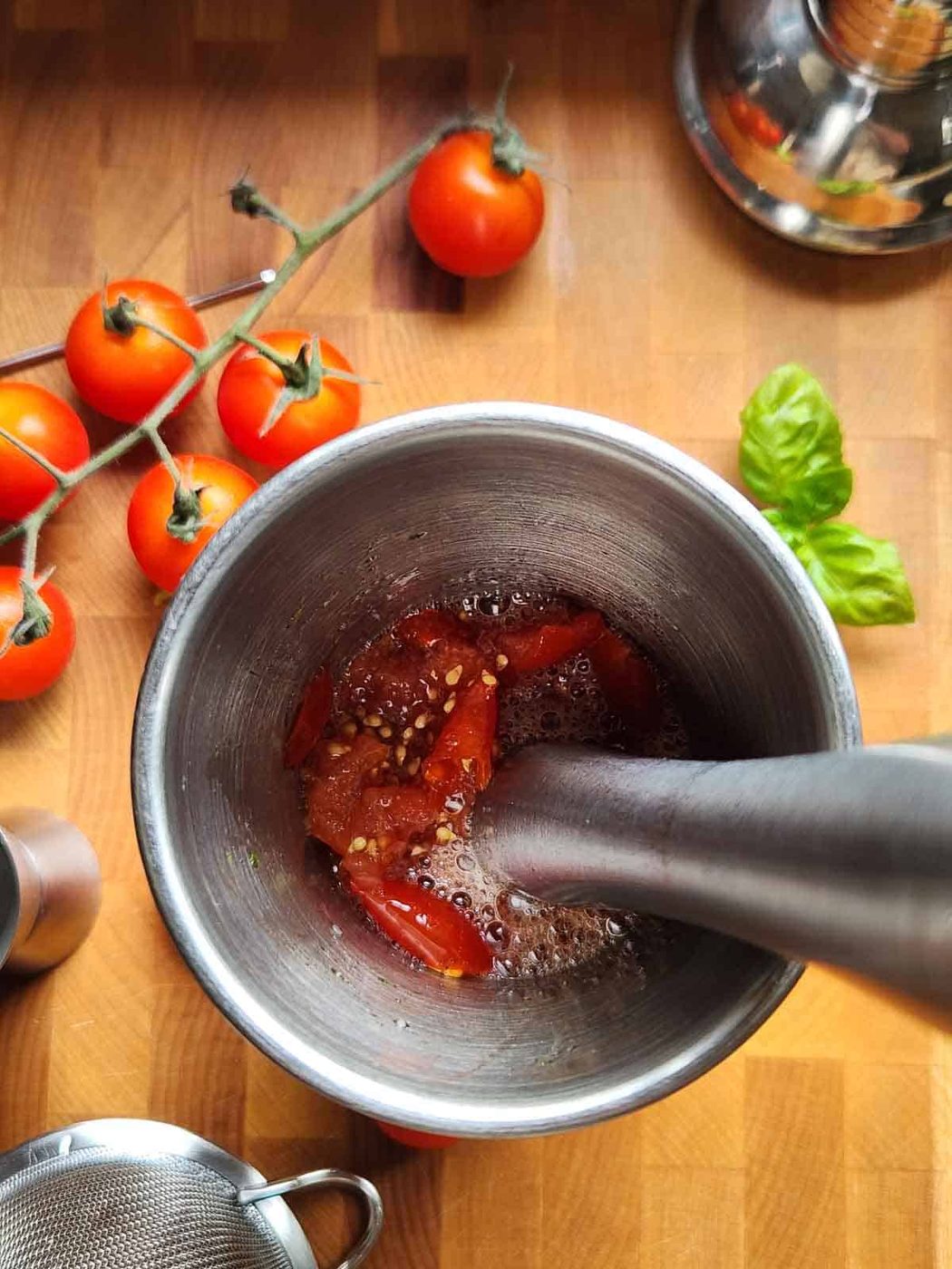 Overhead shot of tomatoes being muddled in a cocktail shaker.