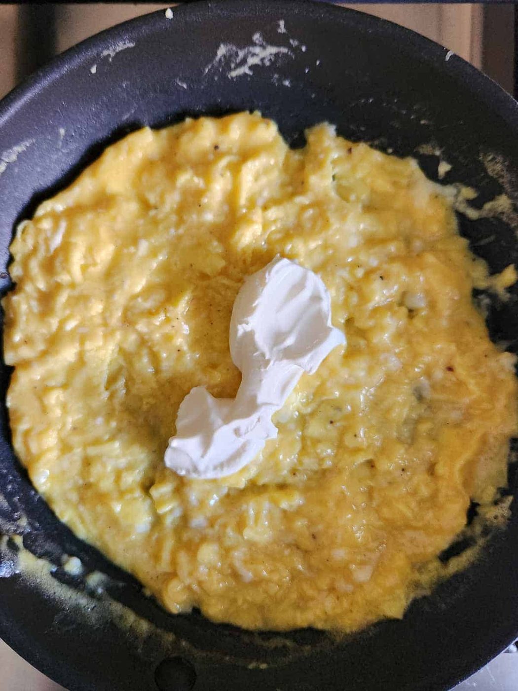 Creme fraiche in the center of soft scrambled eggs in a pan for an omelet.