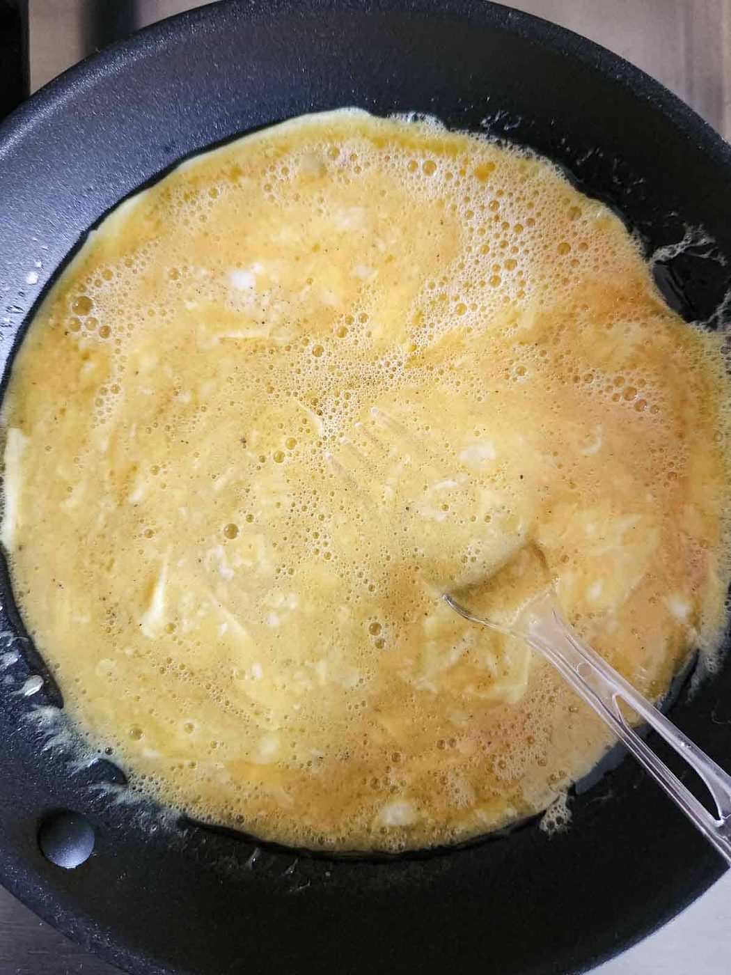A fork swirling eggs in a pan.