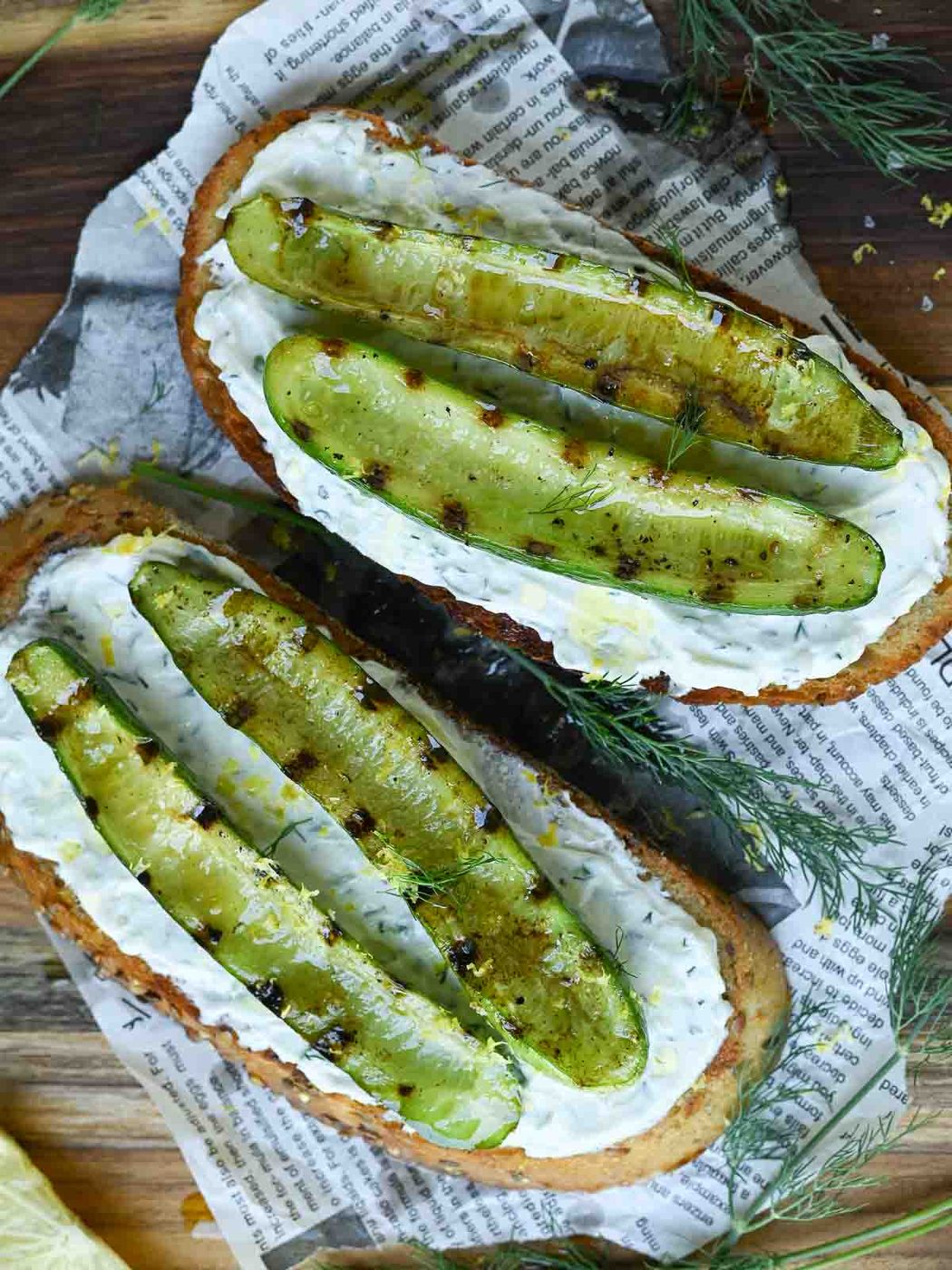 Overhead of grilled cucumber toast with dill on a wooden board.