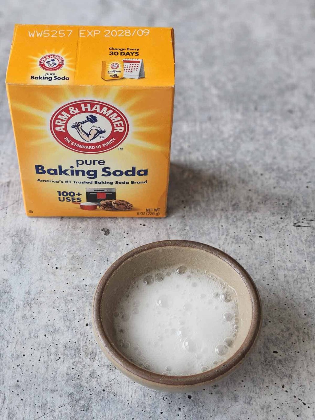Baking soda bubbling in a small bowl on a grey surface.