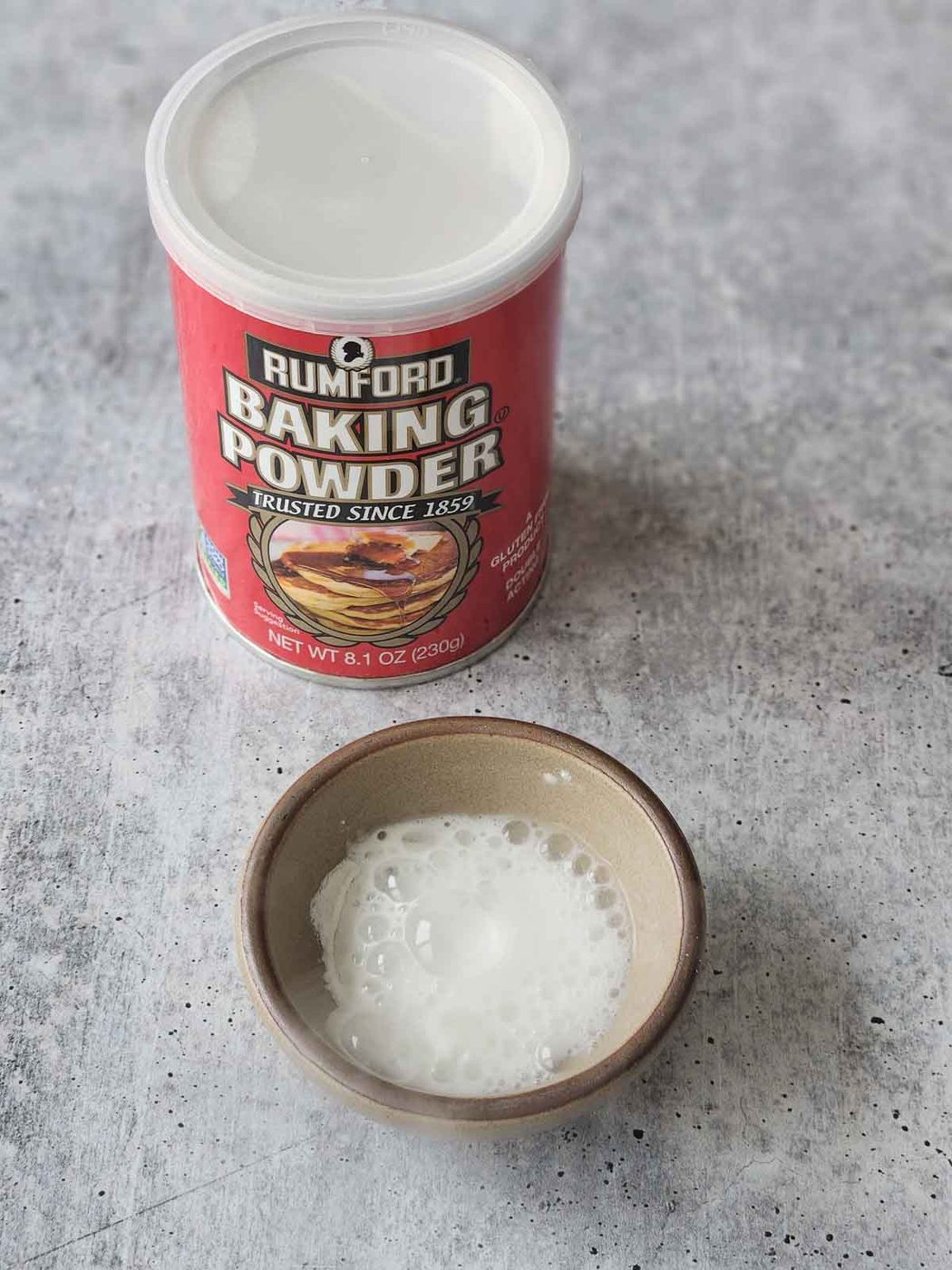 Baking powder bubbling in a bowl with water on a grey surface.
