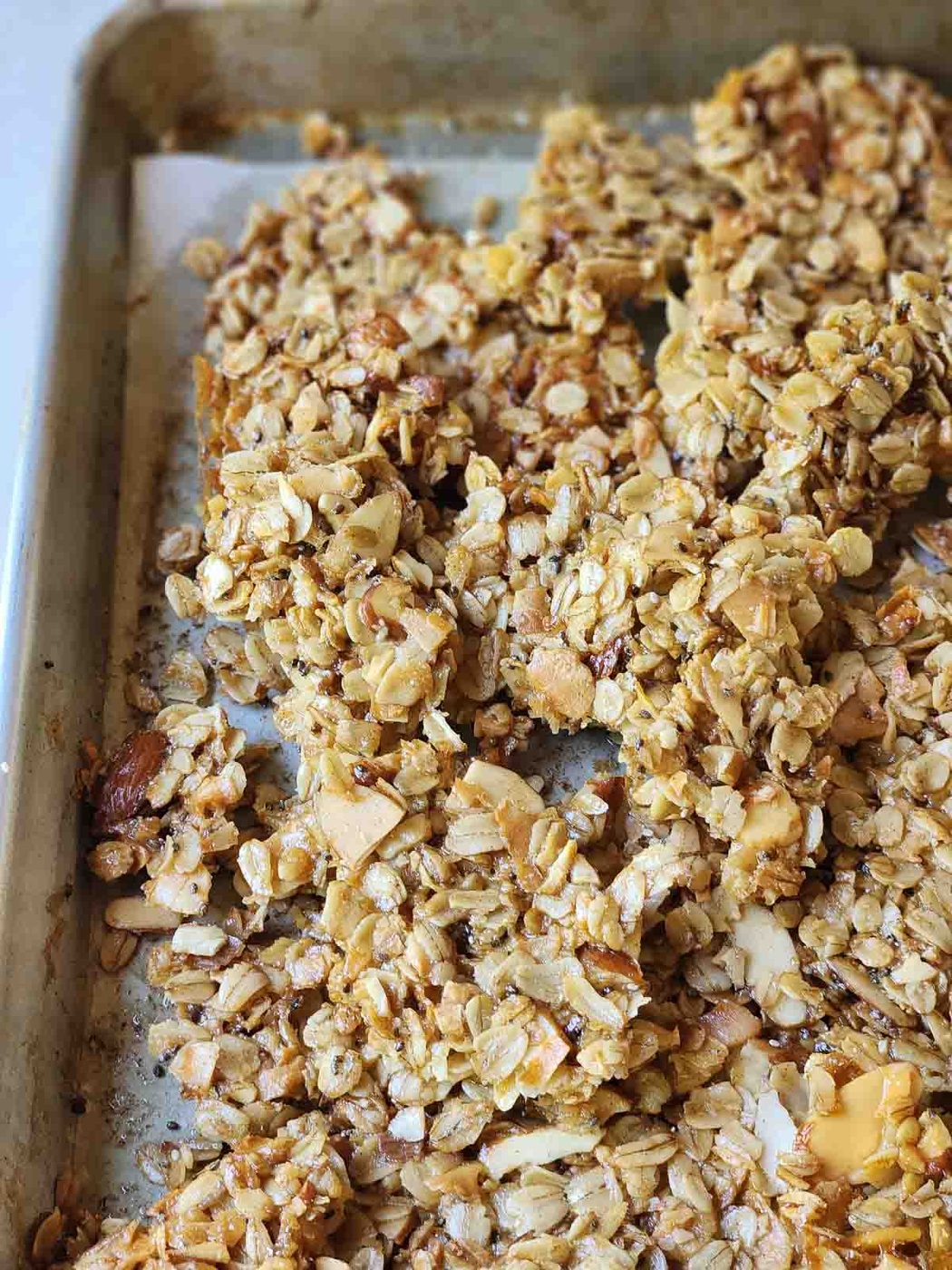 Baked granola in a sheet pan, broken up into clusters.
