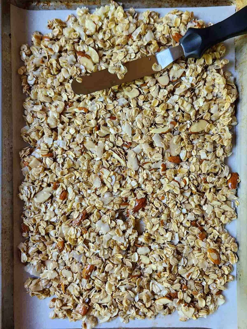 Overview of granola being spread on a sheet pan.