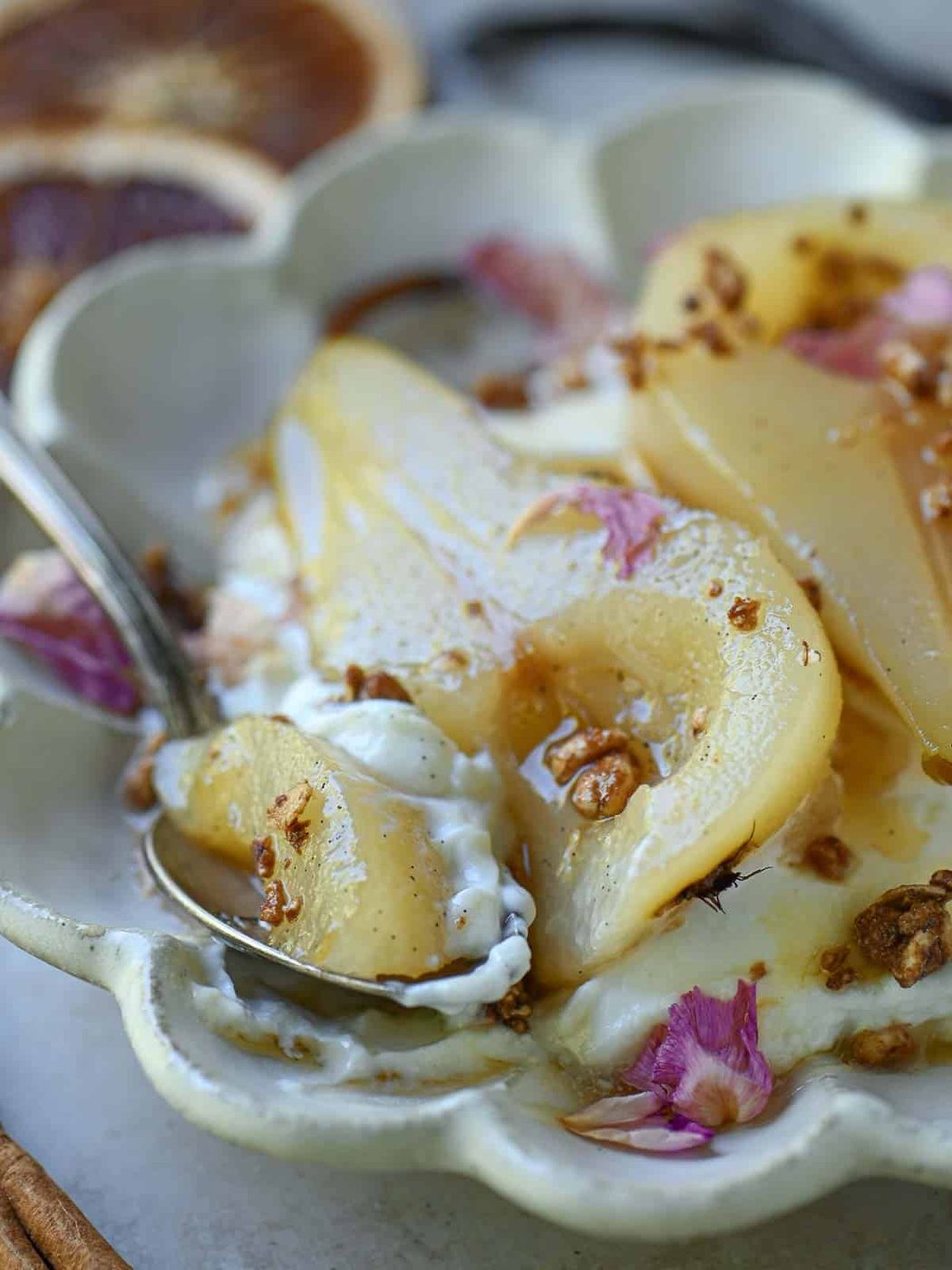 Close up of poached pears with a spoon on the right in a beige plate.