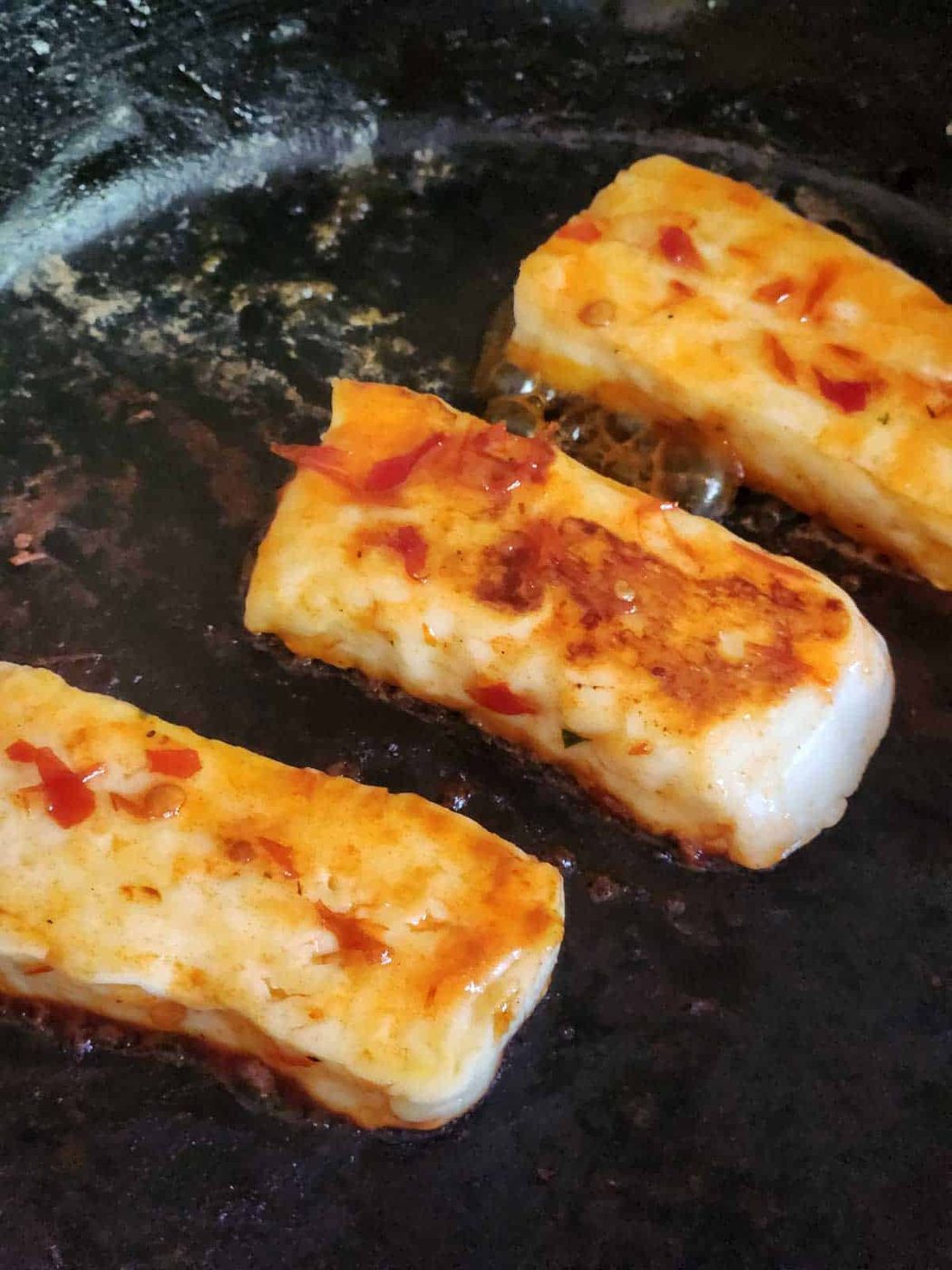 Three pieces of fried halloumi in a black skillet.