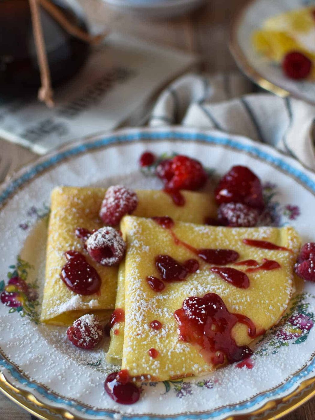 Close-up of stuffed crepes on a flowered plate with raspberry sauce on top.