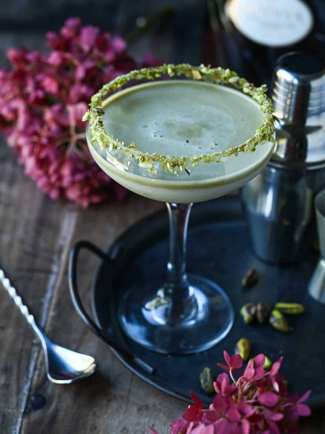 Pistachio martini on a tray with pink flowers next to it.
