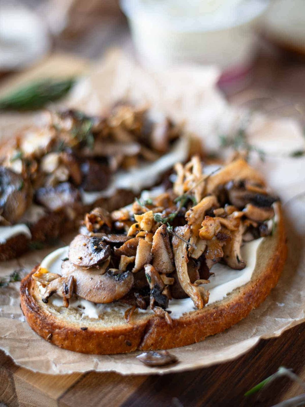 Angled view of 2 slices of mushroom tartine on parchment paper.