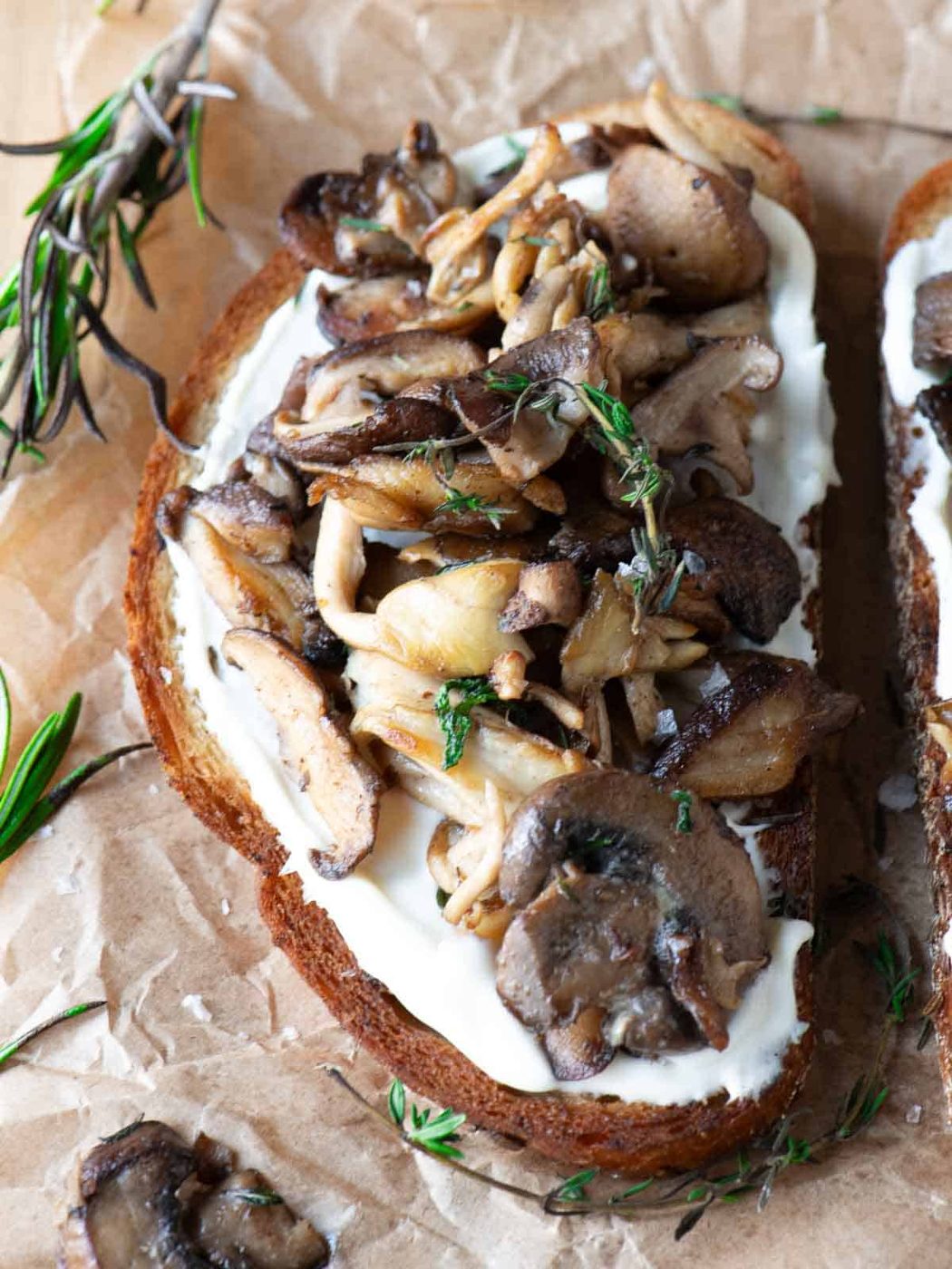 Close-up of mushroom toast with rosemary and thyme on top.