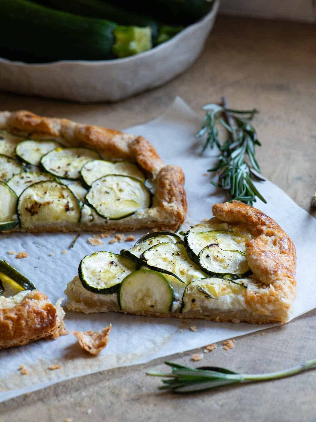 A slice of zucchini galette cut out on parchment paper with rosemary in the background.