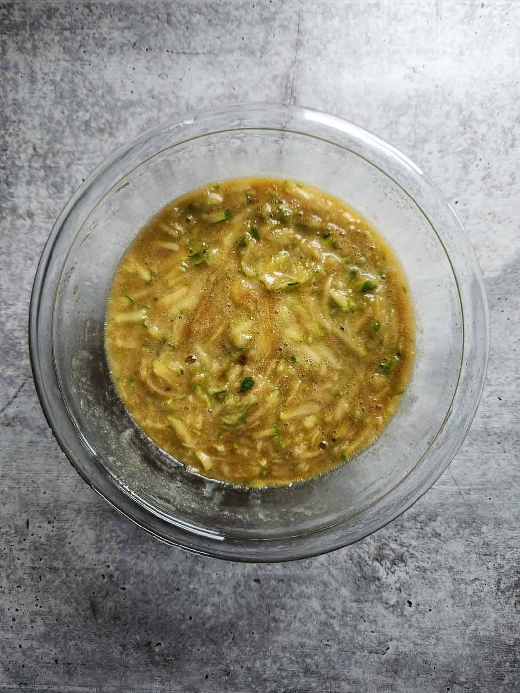 Zucchini muffin batter in a clear bowl.