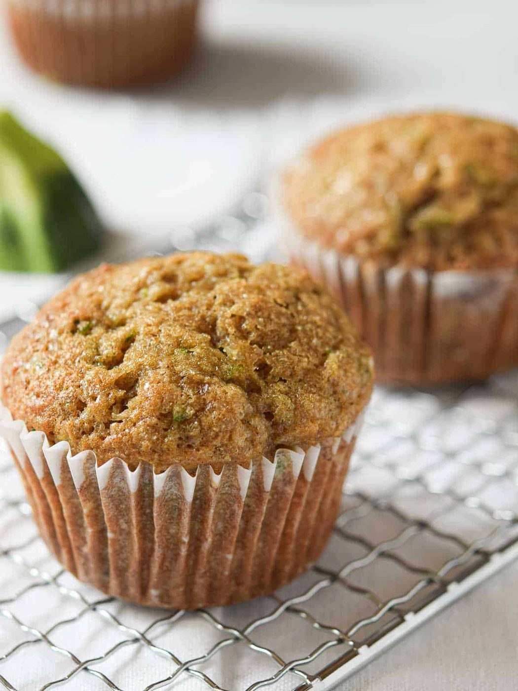 Zucchini muffins on a silver rack over a white surface.