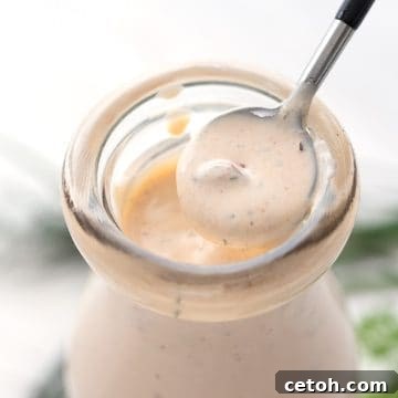 Close up of a spoon lifting some Chipotle Ranch Dressing out of a glass bottle.