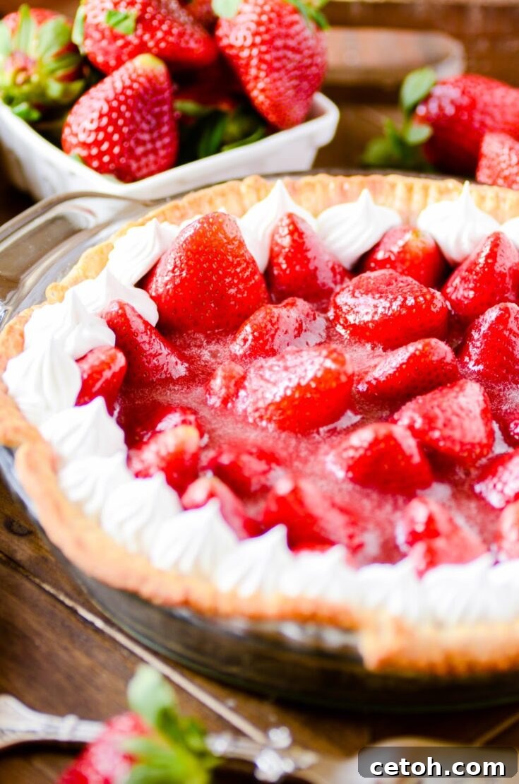 A vertical image of a slice of fresh strawberry pie on a plate, with a background of whole strawberries and a pie in a pan, suitable for Pinterest sharing.