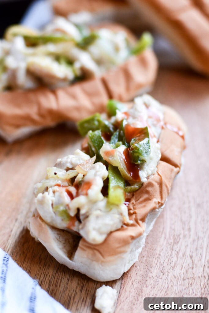 Chicken Philly cheesesteak topped with a drizzle of hot sauce, ready to be eaten.