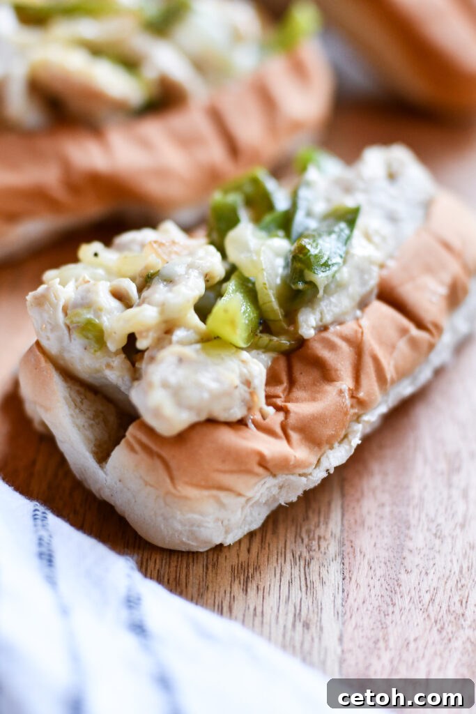 Two halves of a delicious chicken philly cheesesteak sandwich on a wooden cutting board.