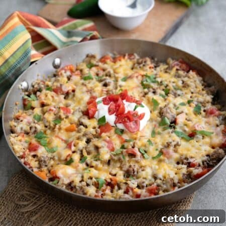Mexican Cauliflower Rice in a skillet with sour cream, cilantro, and chopped tomatoes on top.