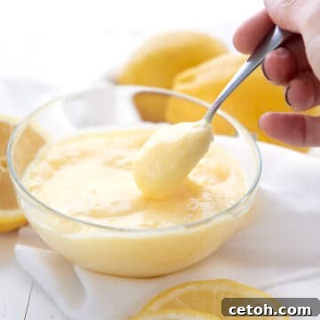 A hand spooning keto lemon curd out of a glass bowl.