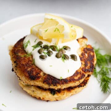 Quick Tuna Cakes 2 Close up shot of tuna patties on a white plate, topped with mayo, lemon, and capers.